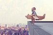  boy with cardboard airplane model and pilot dress looks away on the ledge of a high building. city ​​in the background. concept of dream and imagination.