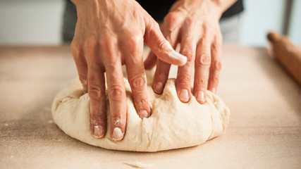 Woman hands knead dough on table in her home kitchen