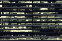 Multi-stories Office Building At Night With Worker Working Overtime. Late Night At Office.  Lighting And Working People Within. Late Night Overtime In A Modern Office Building