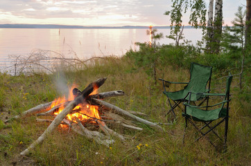 Wall Mural - Summer evening campfire by the river against the setting sun.