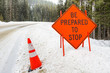 Warning Sign and a Traffic Cone on a Snowy Mountain Road at  the beginning of a Construction Site