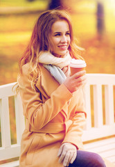 Wall Mural - happy young woman drinking coffee in autumn park