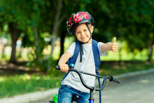 Little Boy Learns To Ride A Bike In Thepark Near The Home. Kid Shows The Thumbs Up On Bicycle. Happy Smiling Child In Helmet Riding A Cycling.