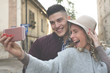 © liderina - Happy couple standing on street an taking self-picture with smart phone.