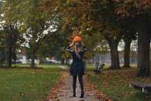 Back View Of A Little Girl In Black Holding An Orange Pumpkin On Her Head