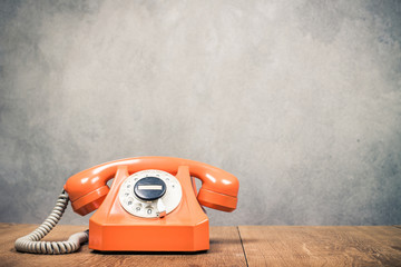 Fototapete - Old orange retro rotary telephone on table front textured concrete wall background. Vintage style filtered photo