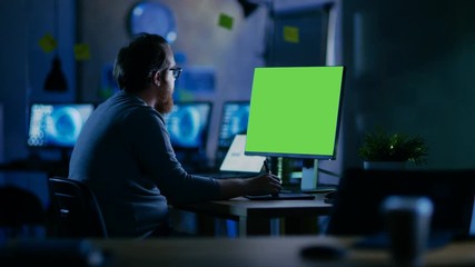 Poster - Creative Bearded Man Works on a Personal Computer with Isolated Mock-up Green Screen. He Works Alone in the Office Late at Night. Shot on RED EPIC-W 8K Helium Cinema Camera.