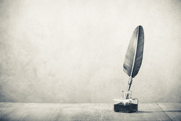 Quill pen with inkwell  on wooden desk. Vintage old style sepia photography