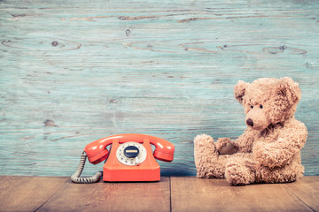 Fototapete - Retro old telephone and Teddy Bear toy near textured wooden wall background. Vintage instagram style filtered photo