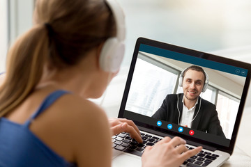 Wall Mural - Man and woman in headphones communicating online by video call, looking at full screen videoconferencing app window, webcam videochat, virtual dating, long distance relationships, close up rear view