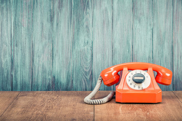 Fototapete - Old orange retro rotary telephone on table front grunge textured wooden wall background. Vintage instagram style filtered photo