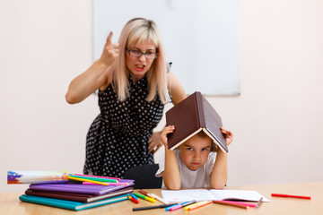 the teacher screams at the little schoolgirl. little girl with a closed book sitting at a desk in the classroom