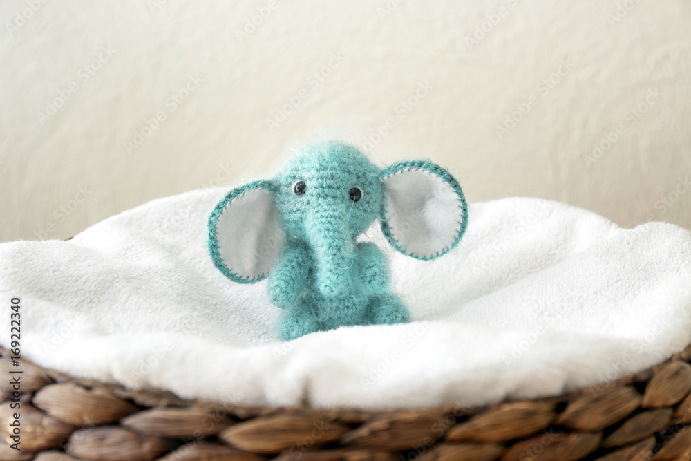 Cute knitted toy elephant in wicker basket on light background