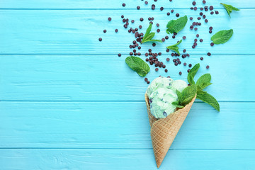 Wall Mural - Composition of delicious mint chocolate chip ice cream in waffle cone and fresh leaves on wooden background