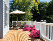 © tab62 - Home cedar deck during bright summer day with blooming garden of flowers