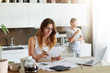 © wayhome.studio  - Attractive female dressed casually, sitting at kitchen table, studying documents, calculating family budget while her husband resting and drinking coffee, standing behind her, looking in window
