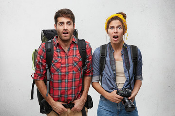 Wall Mural - Astonished horrified couple of young Caucasian tourists carrying heavy rucksacks feeling scared while they didn't make it to catch last train or bus. People, hiking, tourism and traveling concept