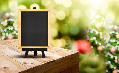Poster - Blackboard with easel on wood table ( food stand ) at blur Christmas tree bokeh light background,Template mock up for display or montage of product or menu