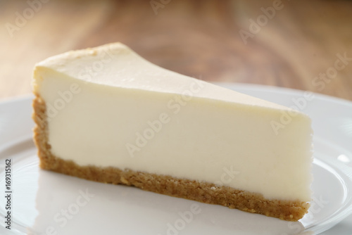 slice of traditional new york cheesecake on white plate on wood table Lerretsbilde