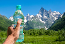 Hand With A Bottle Of Water Against The Background Of The Mountains