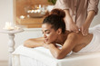 © Cookie Studio - Tender african girl smiling enjoying massage with closed eyes in spa resort.