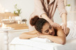 © Cookie Studio - Beautiful african girl smiling enjoying massage with closed eyes in spa salon.