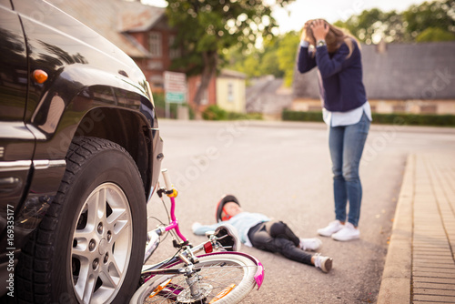 Fotografía Accident. Girl on the bicycle crosses the road in front of a car
