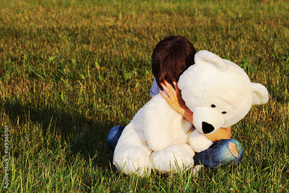 Sad boy sitting outdoors and hugging teddy bear Stock Photo | Adobe Stock