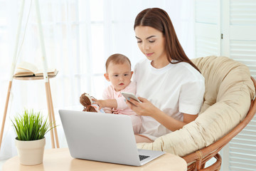 Canvas Print - Young mother holding baby while working in home office