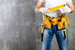 unidentified handyman standing with a tool belt with construction tools and holding roulette against grey background with copyspace. DIY tools and manual work concept