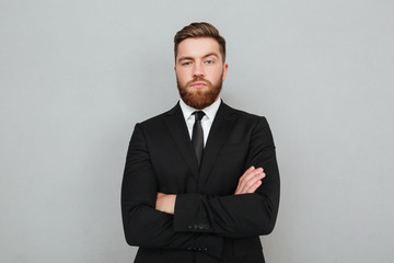 Wall Mural - Confident young businessman in suit standing with arms folded