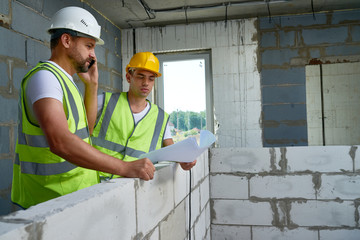 Wall Mural - Portrait of two construction workers wearing hardhats discussing floor plans inside unfinished  building