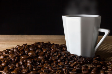 Low key coffee in the darkness. Roasted coffee beans on a wooden table with a glass of white ceramic.