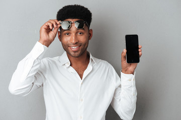 Sticker - Happy african man in sunglasses showing blank screen mobile phone