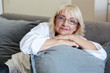 © Drobot Dean - Smiling mature lady sitting on a couch
