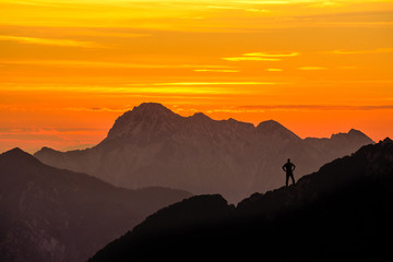 Aufkleber - Happy successful winning man reaching mountain summit. Spectacular layered mountain ranges silhouettes with orange sunset sky.