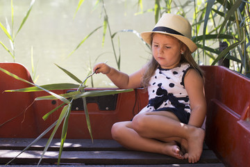 Portrait of sweet little girl in a dress with a hat while sitting in a boat on the lake