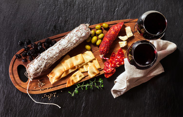 Italian snacks on a wooden board with wine. Whole salami and different types of olives. Traditional Mediterranean table