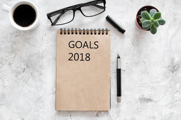 Words Goals for 2018 writting in notebook near glasses and cup of coffee on grey stone background top view mockup
