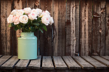 Pink Roses In A Green Bucket Style Container On A Wooden Plank Table.