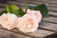 Three Pink Roses On A Weathered Plank Table.