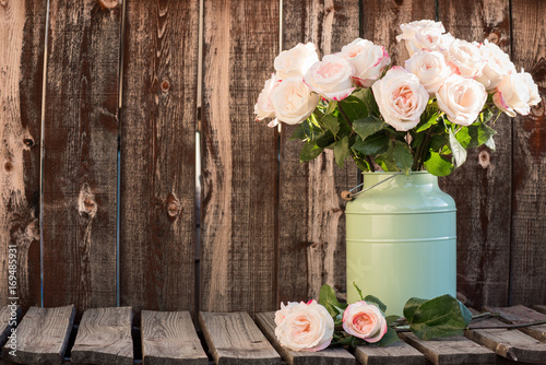 Plakat Różowe róże w pojemniku zielony wiadro na drewnianym stole.
