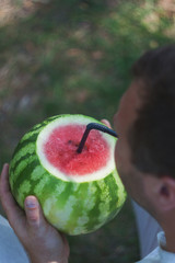 Wall Mural - A young man holds a whole watermelon with a straw for drinking, a cocktail. The concept of healthy nutrition and vegetarianism