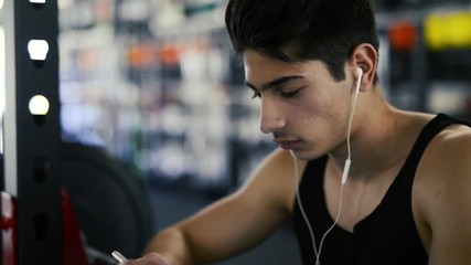 Poster - Hispanic man in gym resting, holding smart phone,listening music