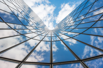 blue sky and white clouds reflecting in a curved glass building