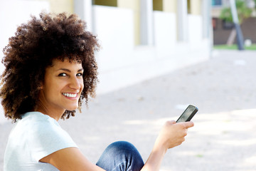 Wall Mural - Smiling woman sitting outdoors holding smart phone