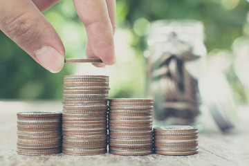 Hand putting coin stack with blurred background jar and green leaf, Save money and investment concept