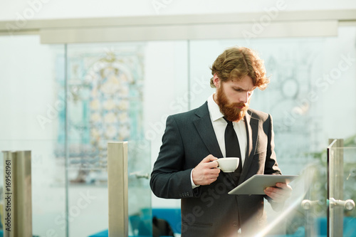 Fotomural Bearded trader with cup of tea and tablet reading online news in the morning