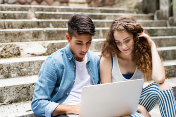 Teenage students with laptop sitting on stone steps.