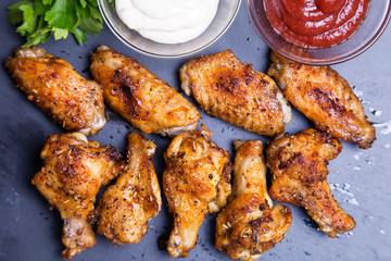 Chicken wings of a barbecue with two sauces on a black board. Close-up. Selective focus.